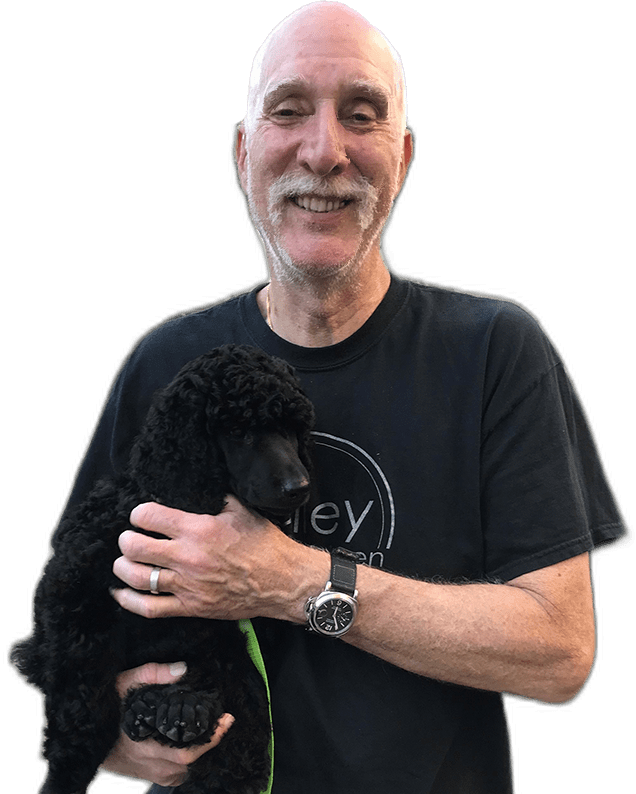 A man holding a black poodle dog.