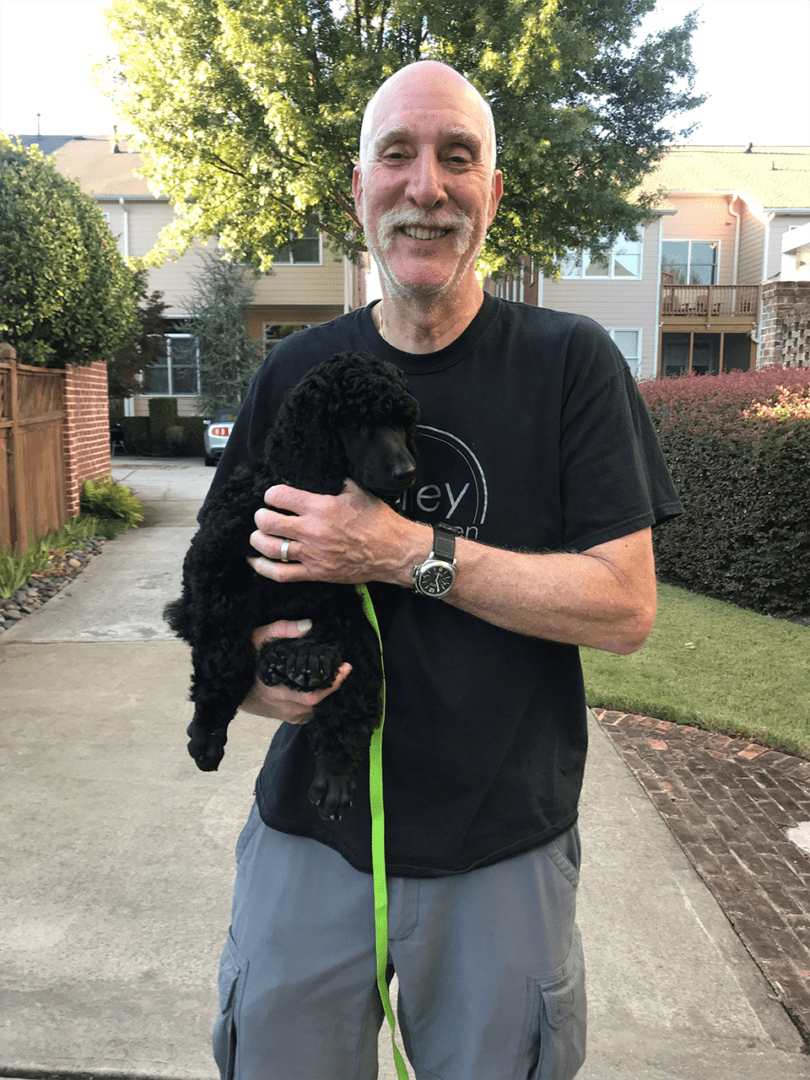 A man holding his dog while standing on the sidewalk.